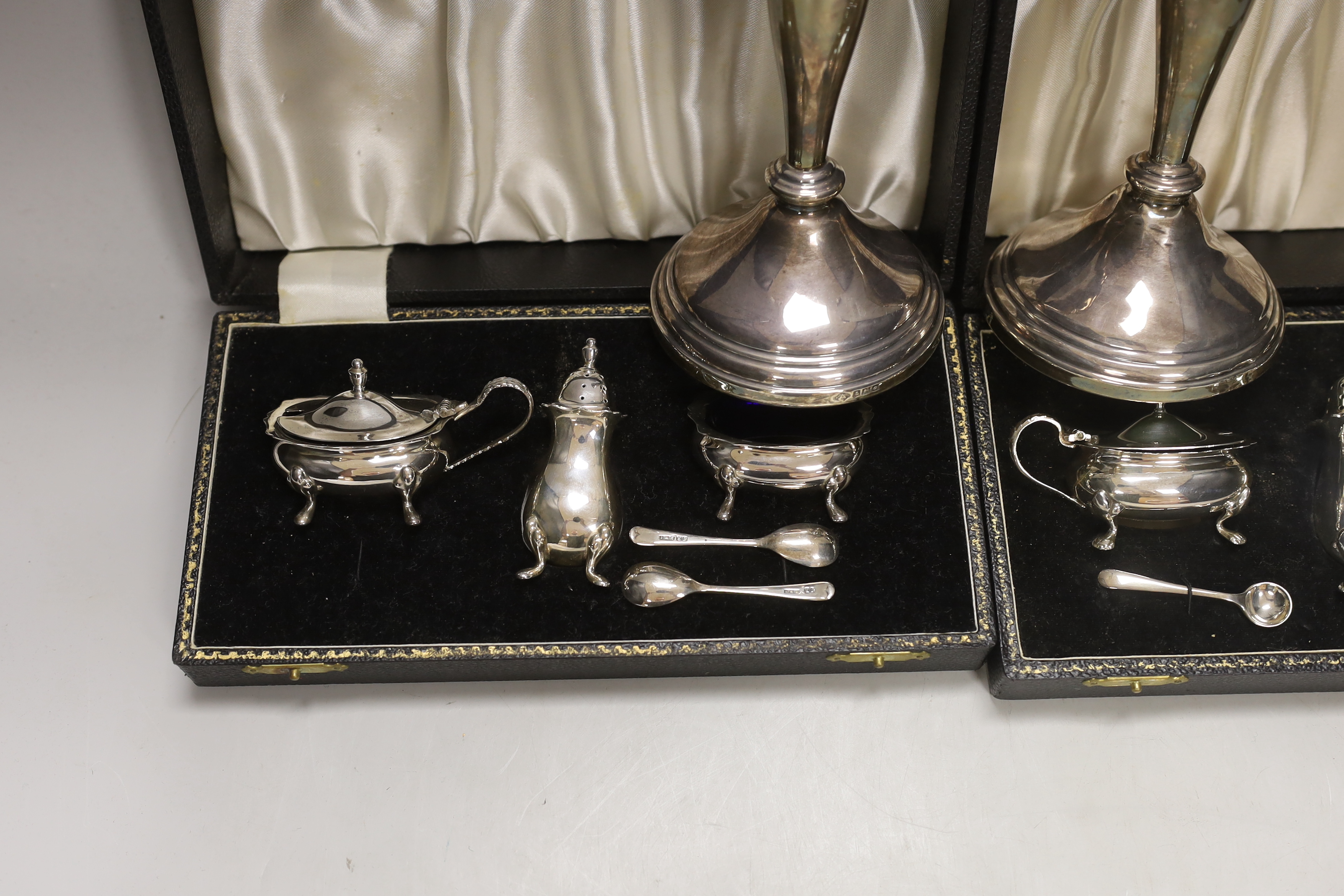 Two modern cased silver three piece cruet sets, with spoons and a pair of modern silver candlesticks, 19.5cm, weighted.